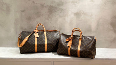 Two Louis Vuitton Keepall duffle bags in Monogram canvas on a stone ledge.