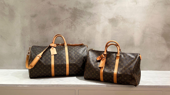 Two Louis Vuitton Keepall duffle bags in Monogram canvas on a stone ledge.